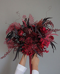 red and burgundy coloured bouquet held with two female hands