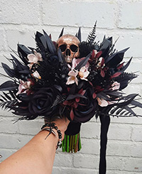 dark coloured bouquet with a few white flowers and a decorative skull held by one female hand