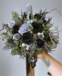 bouquet with lots of greenery, native plants, black roses and crystals held by one female hand